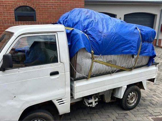 Mattress strapped under a blue tarp on a small truck